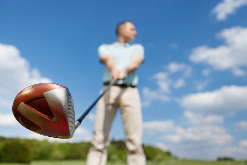man holding golf club against blue sky at a low angle view