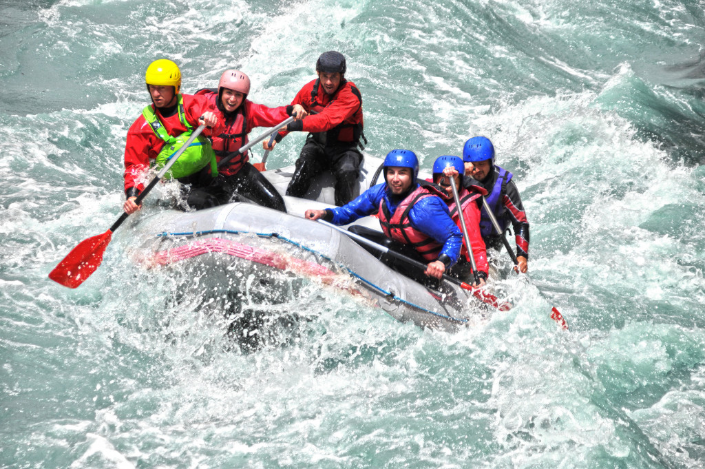 Six people on board a raft going through rough waters in a river.